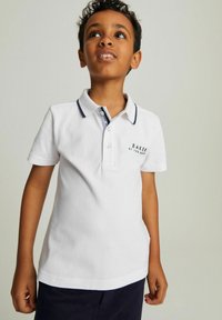 Biely polo tričko s krátkym rukávom a námorníckym golierom a zapínaním na gombíky. Na hrudi sa nachádza logo "BAKER by Ted Baker" v tmavom texte.