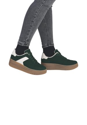 Green suede sneakers with white accents, thick beige sole, and laces. Worn with grey skinny jeans and black socks, showing side profile.