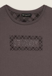 Camiseta gris de manga corta con un patrón texturizado y un logotipo "FREDDY" con tachuelas en la parte delantera. Diseño de cuello redondo, tela suave y estilo casual.