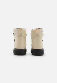 Beige ankel støvler med en teksturert overflate, svarte gummisåler og doble stropper; har et lite logo på hælen.