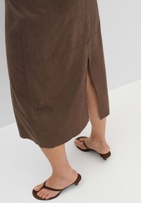 Gonna midi in suede marrone con uno spacco laterale, caratterizzata da una texture liscia. Abbinata a semplici sandali con tacco marroni.
