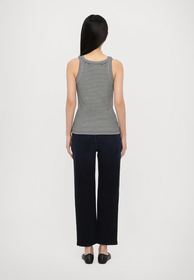 Stribet tanktop i sort og hvid, tætsiddende design med en rund halsudskæring. Kombineret med brede mørkeblå jeans og sorte flade sko.