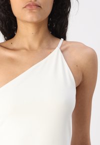 Asymmetrical white top with a single strap, made of smooth fabric, featuring a minimalist design and a fitted silhouette.