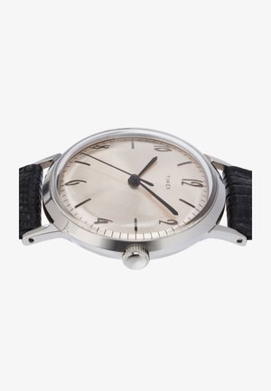 Srebrnokovinski okrogli ura s telesom iz nerjavečega jekla, svetlo srebrnim številčnikom, črnimi kazalci in teksturiranim črnim usnjenim trakom. Ima tudi krono.