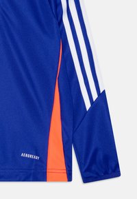 T-shirt de sport bleu avec un panneau latéral orange, des rayures blanches sur les manches et le logo "AEROREADY" près de l'ourlet. Texture de tissu lisse.