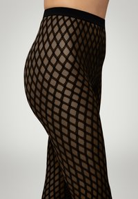 Leggings in rete nera con motivo a diamante, una vita larga e una texture trasparente, che enfatizza il design geometrico.