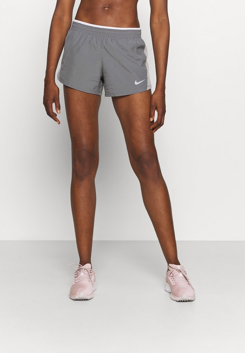 Pantalones cortos deportivos grises con cinturilla blanca, que presentan un logo de Nike en el lado izquierdo. Llevados con zapatillas de correr rosa claro.