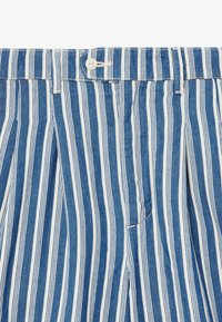 Modré a biele pruhované nohavice s gombíkovým pásom, s plisovaným dizajnom a výraznými vertikálnymi pruhmi na tkanine pripomínajúcej denim.