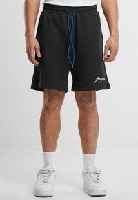 Mustat puuvillashortsit, joissa on sileä pinta, sininen nyöri ja valkoinen logo- yksityiskohta helman kohdalla. Yhdistettynä valkoisiin urheilukenkiin ja sukkiin.