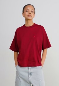 Tricou din bumbac burgund cu guler rotund și mâneci scurte. Prezintă un mic detaliu cu logo pe piept. Asortat cu pantaloni din denim deschis.