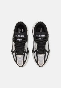 Baskets noires et grises avec des textures en mesh et synthétiques, présentant un design à lacets et un logo bien visible sur la languette. Semelle arrondie.