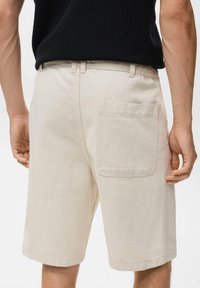 Bermudas beige con un bolsillo trasero, fabricadas en un tejido resistente. Presentan una cintura con trabillas y un corte holgado. Diseño minimalista.