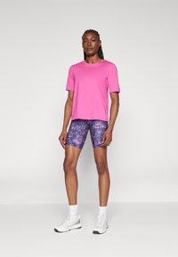 Pink short-sleeve athletic shirt paired with textured purple patterned cycling shorts. White sneakers with gray accents complete the outfit.