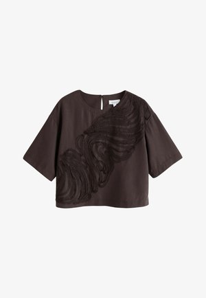 Blouse courte marron foncé à manches courtes avec col rond et motif tourbillonnant texturé abstrait en diagonale sur le devant.