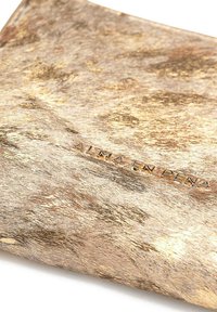 Material texturizado de color dorado con patrones sutiles. Presenta el texto en relieve "ALMA EN PEÑA", mostrando un diseño suave y elegante.