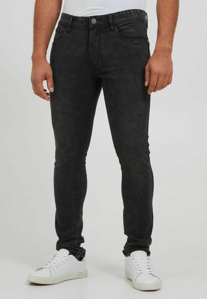 Crne slim-fit traperice s pet džepova, zip zatvaranjem i kontrastnim šavovima. U kombinaciji s bijelim tenisicama.
