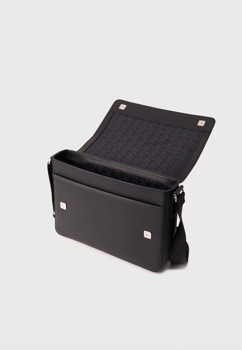 Zwarte rechthoekige boodschappentas met geopende klep, magnetische sluitingen, patroon aan de binnenvoering en verstelbare schouderriem.