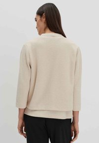 Beiger Strickpullover mit Dreiviertelärmeln und lockerer Passform. Verfügt über eine strukturierte Oberfläche und ein geschichtetes Saumdesign.