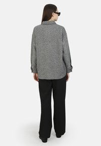 Harmaa herringbone-kuosiset paitajakku, jossa on kaulus, väljät istuvuus ja napitettu hihansuu, yhdistettynä mustiin leveälahkeisiin housuihin ja mustiin kenkiin.