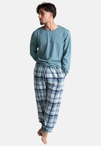 Langsleeve teal top met grafische details, gecombineerd met plaid pyjamabroek van zachte stof in lichtblauw, marineblauw en wit.
