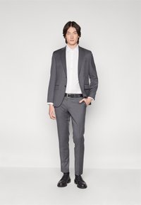 Gray tailored suit with a single-button jacket, matching trousers, and a white button-up shirt. Black belt and polished black shoes.