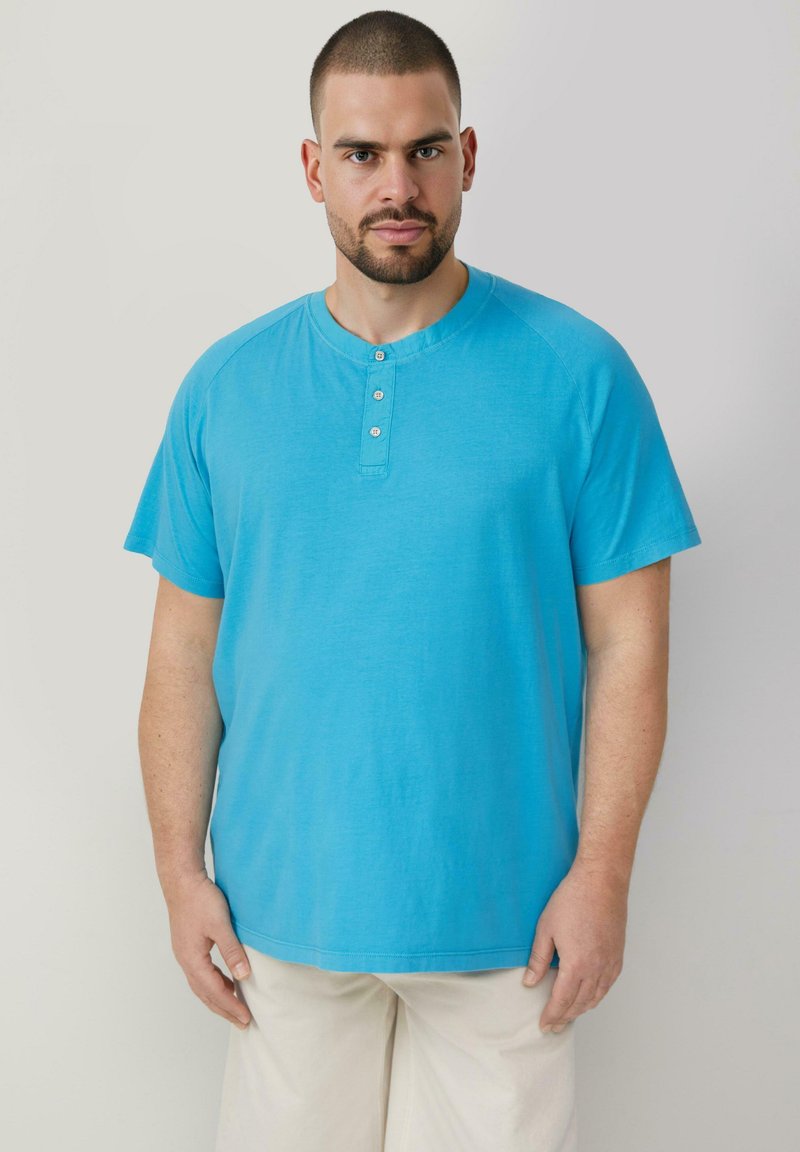 Turkusowa koszulka z krótkim rękawem, z okrągłym dekoltem i listwą na trzy guziki. Miękka tkanina, prosty krój i minimalne detale w szwach.