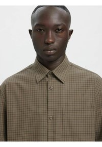 Brun ruteskjorte laget av lett stoff, med spiss krage, knappestolpe foran og en enkelt brystlomme.