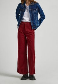 Farkkutakki tummansinisena, valkoinen t-paita printillä, leveälahkeiset punaiset housut, mustat paksupohjaiset kengät, etukuva, sileä kangas, rento tyyli.