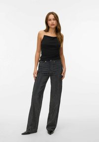 Sort ærmeløs bluse med en lige halsudskæring, parret med brede sorte jeans med et subtilt mønster. Spidse sorte hæle fuldender looket.