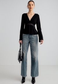 Bluza neagră cu mâneci lungi, cu detaliu din dantelă la talie, asortată cu blugi largi de culoare albastru deschis și cizme negre cu vârf ascuțit. Geantă neagră.