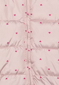 Doudoune rose clair avec une fermeture éclair verticale et de petits motifs de cœurs roses sur tout le tissu. Texture lisse avec des sections matelassées.