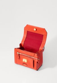 Rød læder håndtaske med tekstureret overflade, lynlåslomme foran og trykknaplukning. Indvendigt foret med bordeaux stof. Kompakt design.