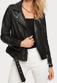 Czarna skórzana kurtka motocyklowa z zamykanymi kieszeniami, pikowanymi akcentami na ramionach oraz regulowanym paskiem w talii. Noszona na czarnej bluzce.