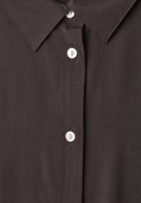 Devant de chemise marron foncé avec des boutons blancs et un col pointu, montrant trois boutons attachés.