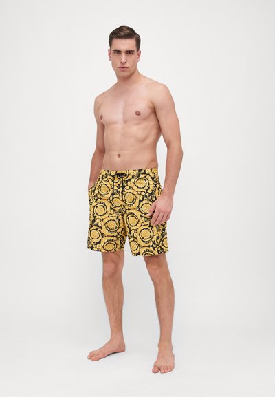 Gula badshorts med ett svart blommönster, med en bekväm elastisk midja och sidfickor. Avslappnad knä-lång design.