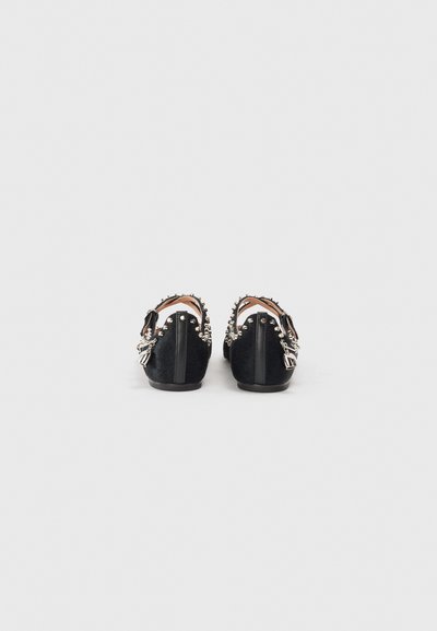 Chaussures noires avec une surface texturée, ornées de clous et de pointes argentés à l'arrière, et à semelle plate. Détail de la sangle inclus.