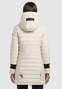 Hvid quiltet pufferjakke med hætte, ribbede sorte manchetter og logo detaljer. Har en tætsiddende pasform og en længere bagdel for ekstra dækning.