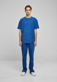 Blå frottéantrekk bestående av en løs T-skjorte og matchende bukser. Glatt tekstur, avslappet design og hvite sneakers.