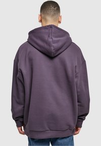 Sweat à capuche violet surdimensionné avec un cordon de serrage, des poignets et un ourlet côtelés. Texture lisse, avec un design simple sans motifs ni accents.