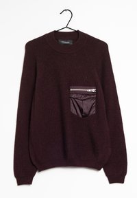 Pull bourgogne avec un col rond et des manches raglan. Présente une poche zippée en tissu contrasté sur le devant. Matière à maille texturée.