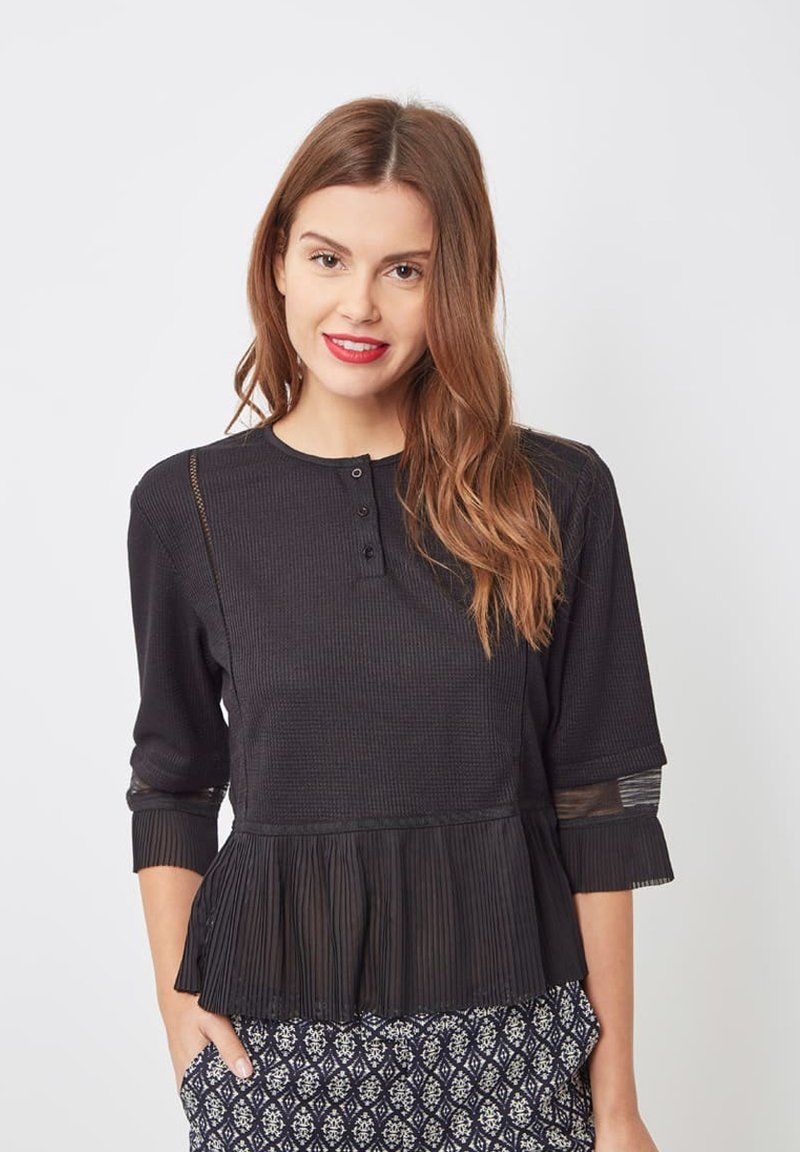 Top negro con mangas de tres cuartos, cuerpo texturizado, dobladillo peplum acanalado y acentos transparantes en las mangas. Estilizado con pantalones de patrón.