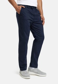 Pantaloni chinos blu navy in cotone, con davanti piatto, tasche laterali e vestibilità comoda, abbinati a sneaker grigio chiaro.