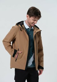 Bruine waterdichte jas met een zwarte capuchon. Kenmerken zijn zijzakken, verstelbare manchetten en een soepele textuur. Draag het over een teal shirt.