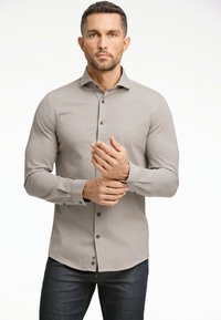 Camicia grigia chiaro a maniche lunghe con bottoni, dal tessuto morbido, dotata di bottoni scuri e colletto classico, abbinata a jeans di denim.