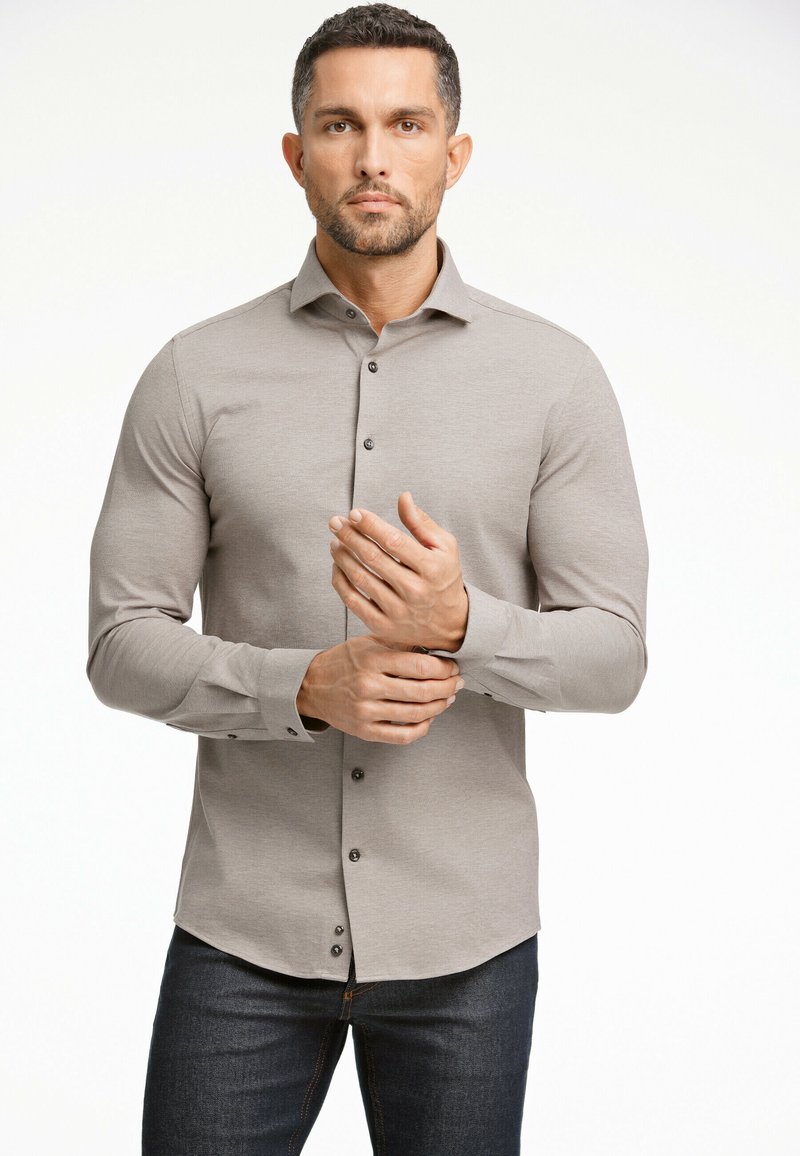 Camicia grigia chiaro a maniche lunghe con bottoni, dal tessuto morbido, dotata di bottoni scuri e colletto classico, abbinata a jeans di denim.