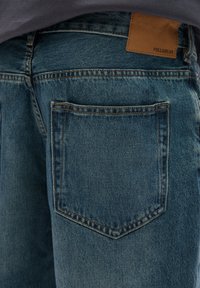 Blue denim jeans with a straight cut, featuring a rectangular back pocket and a brown leather patch with "PULL&BEAR" branding.