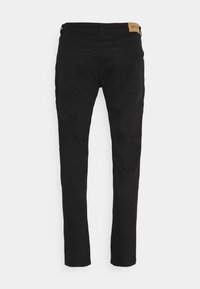 Svarta slim-fit jeans visade bakifrån med två bakfickor och en brun läderlogotyp på midjan.
