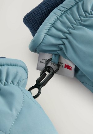 Gant en bleu clair isolé avec un épais poignet en tricot marine, doté d'un clip noir et d'une étiquette d'entretien attachée à l'intérieur.