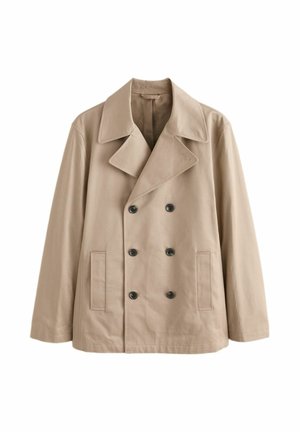 Camicia blu con colletto sotto un maglione rosso lavorato a maglia con un cappotto beige sopra.