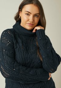 Navyblauer gestrickter Rollkragenpullover mit strukturierten Zopfmustern und übergroßen Ärmeln, sowie einem gerippten Kragen und Bündchen.